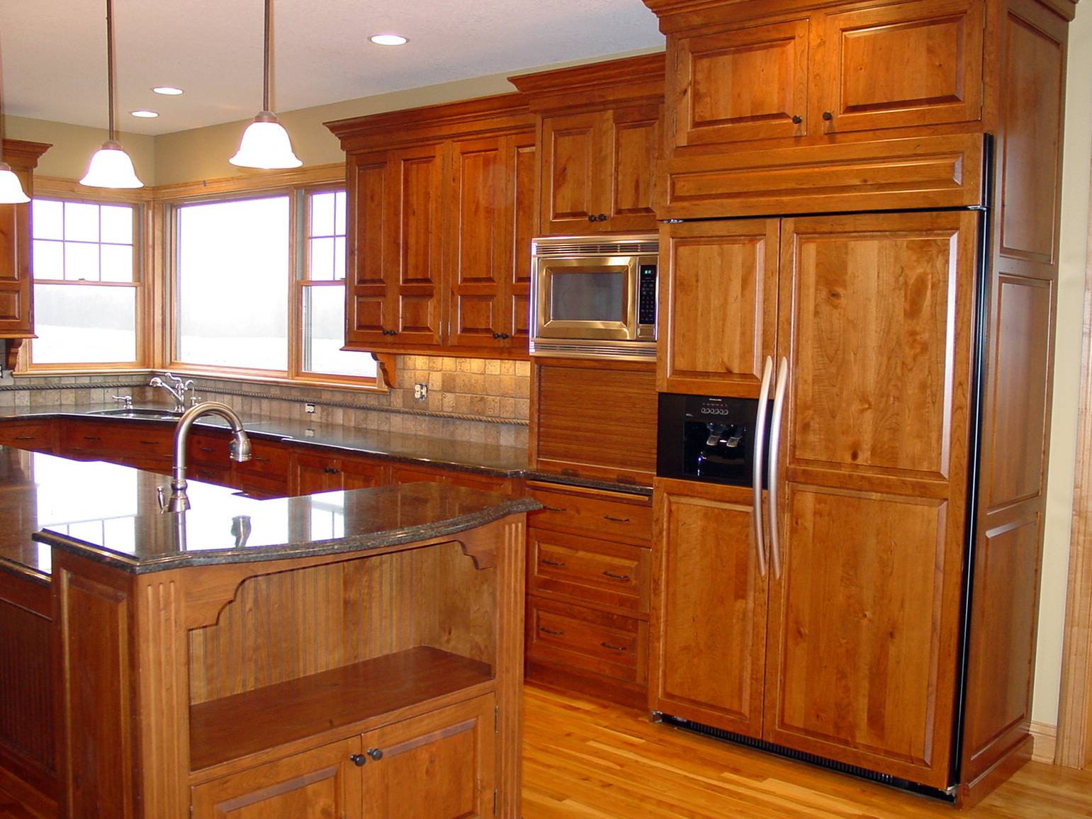 New kitchen with wood cabinets, stone countertops and custom panel fridge